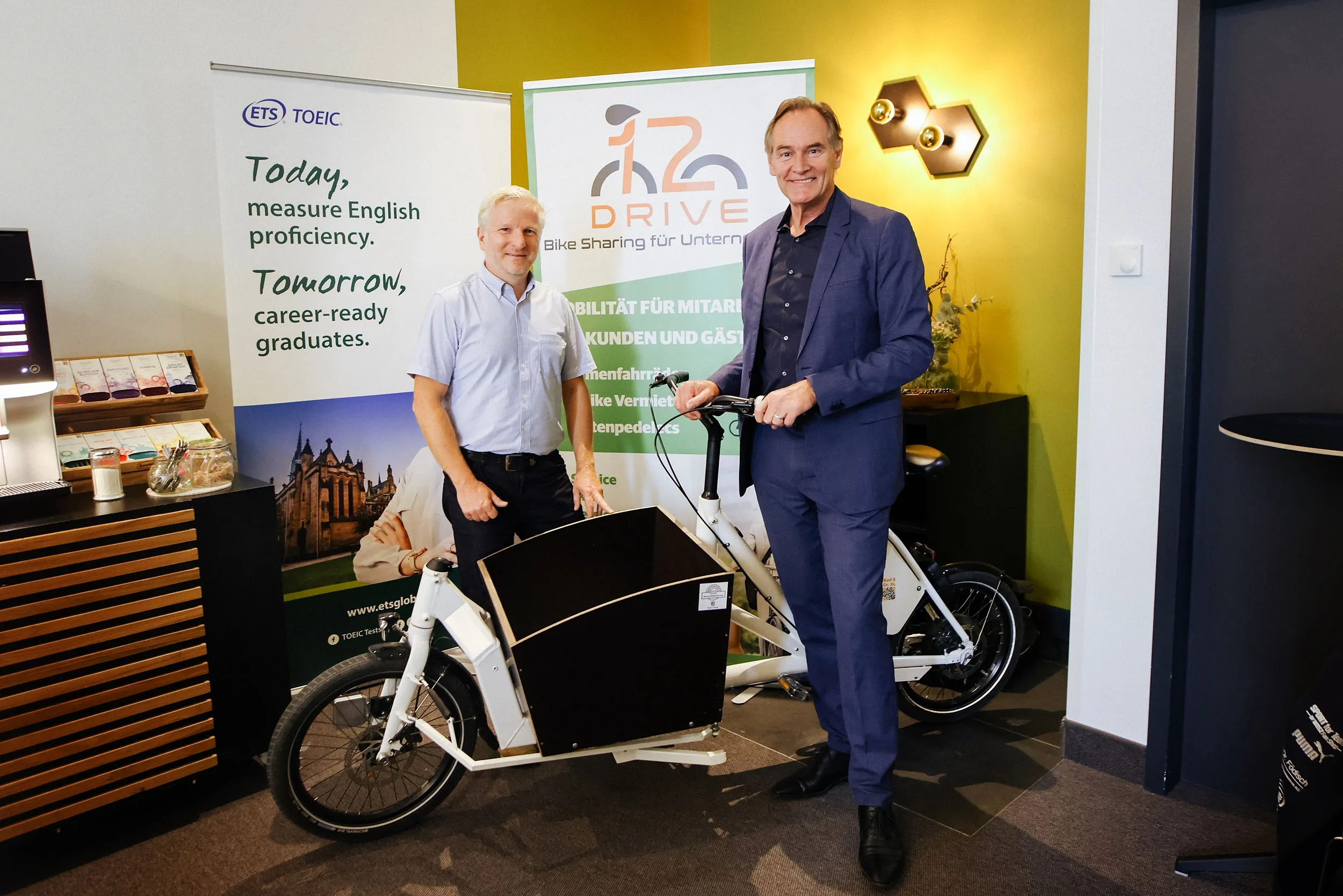 Burkhard Jung und ein Clubmitglied mit einem Lastenrad vor Roll-ups von ETS TOEIC und 12drive